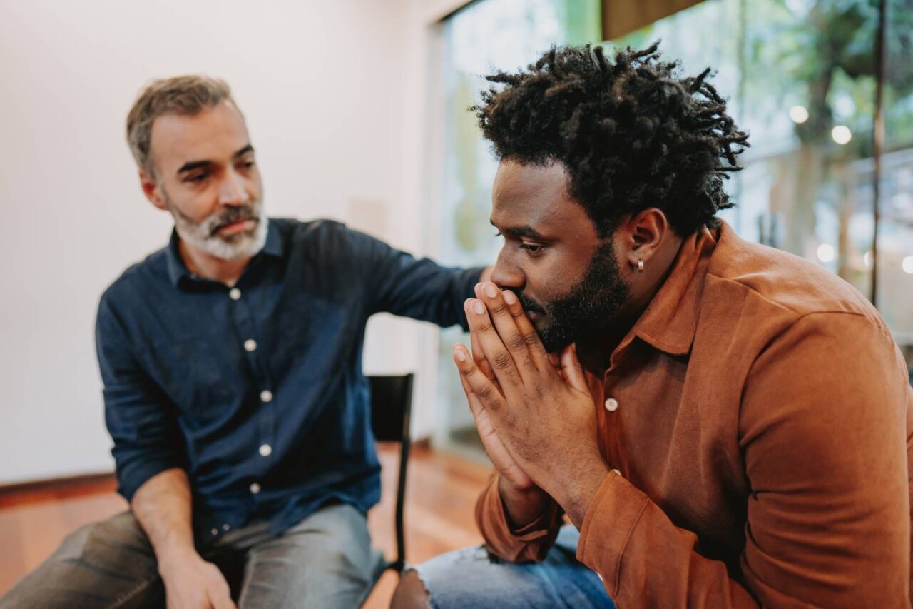 Image of two men, in a support group with slight smiles indicating the importance of men getting help for their mental health.